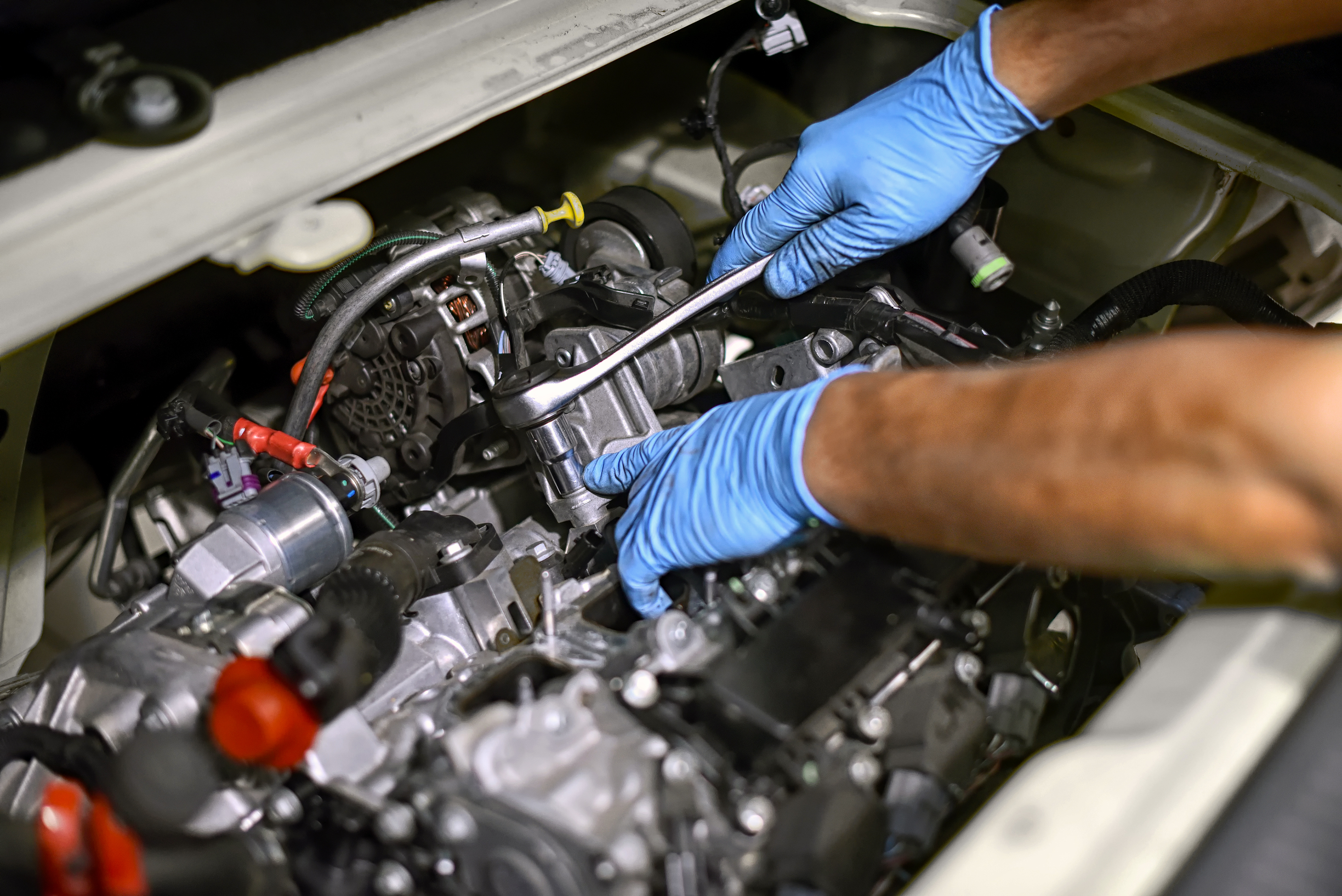 Hands of a mechanic working on a car engine Hands of a mechanic wearing blue gloves working on a car engine with a spanner in a concept of maintenance and repair