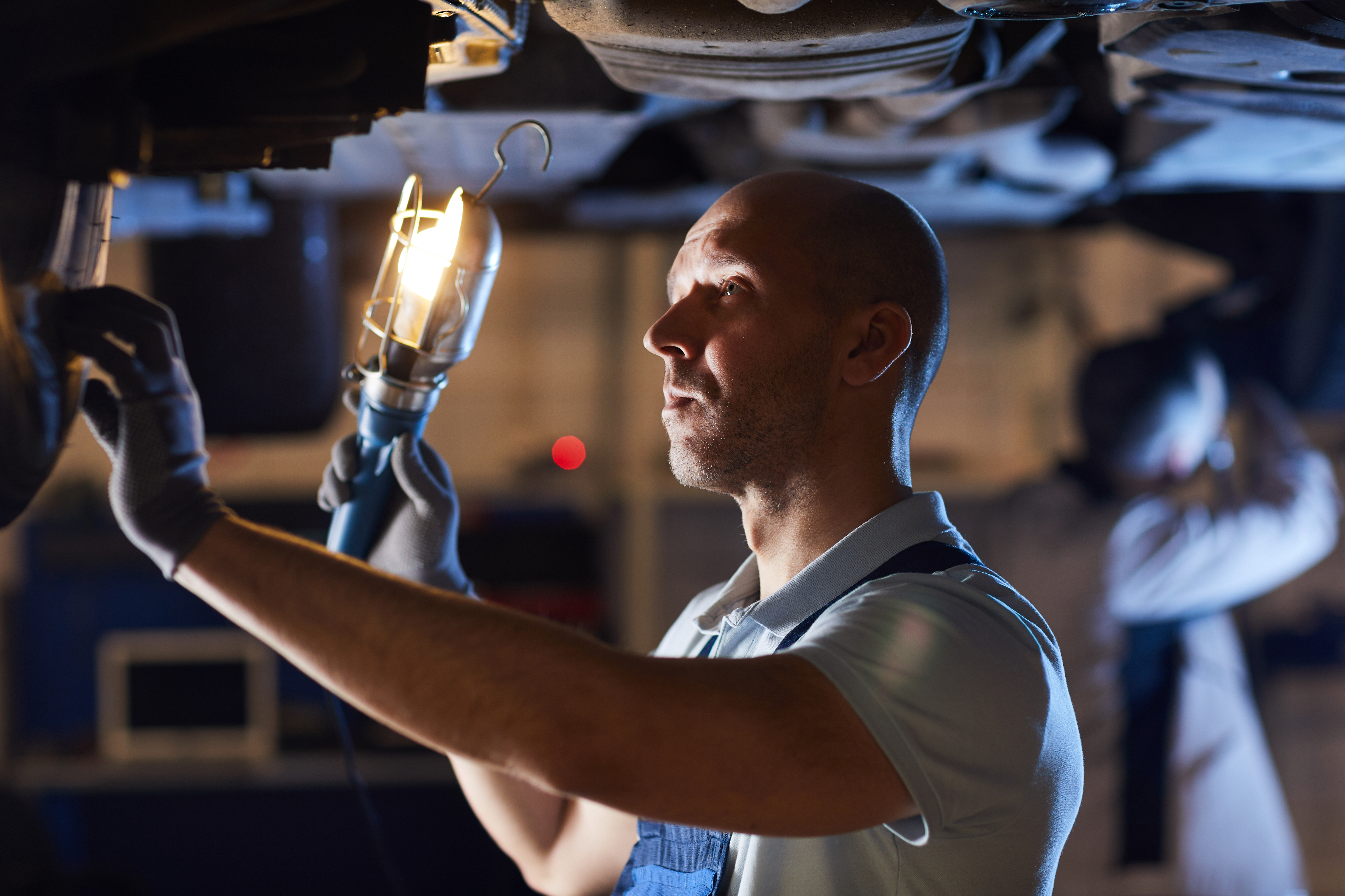 Mechanic Fixing Car Waist up portrait of bald car mechanic inspecting vehicle while holding flashlight lamp under car lift, copy space